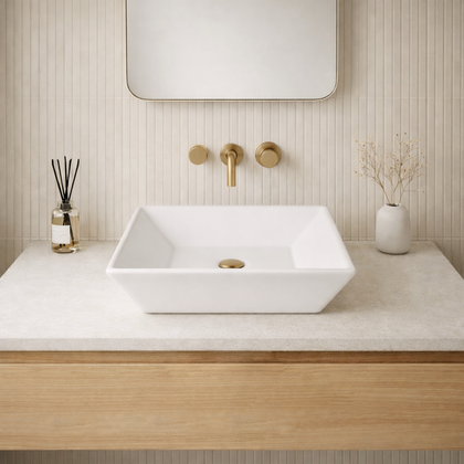 Square modern white ceramic vessel sink on a minimalist bathroom countertop with gold fixtures and decor.