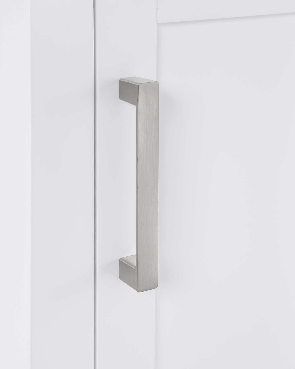 Close-up of a sleek brushed nickel cabinet handle on a white cabinet door.